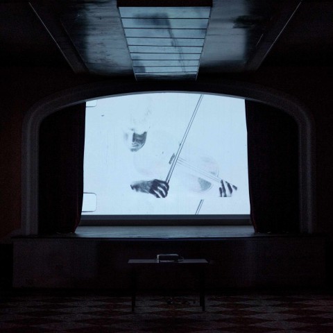 Solarised film projection of violinist shown on cinema screen