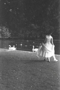 Photo of Louise Hughes wearing a dress that captures the spirit of a swan as she walks along a river bank with swans