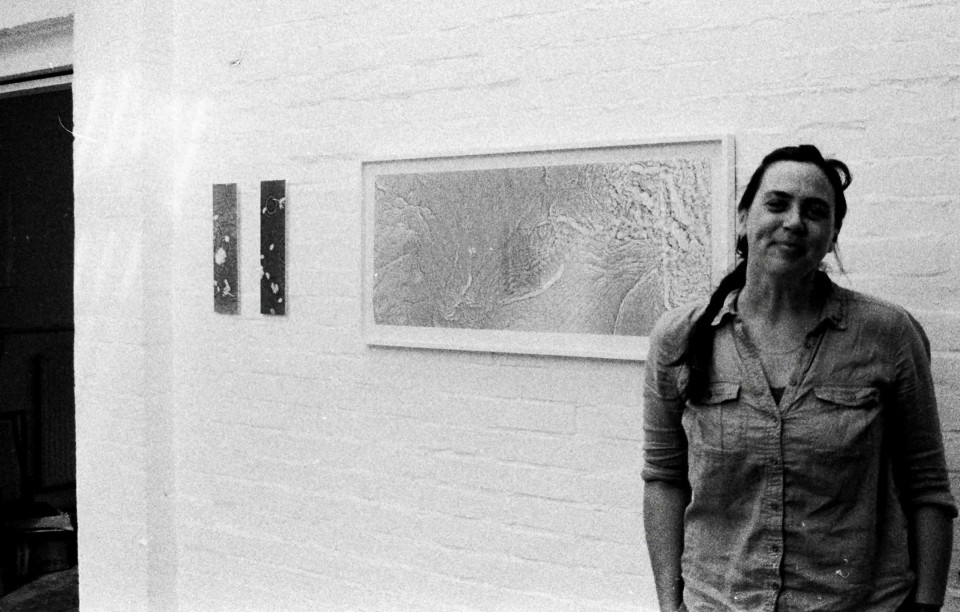 Photo of Kate posing next to exhibition artwork hanging on walls