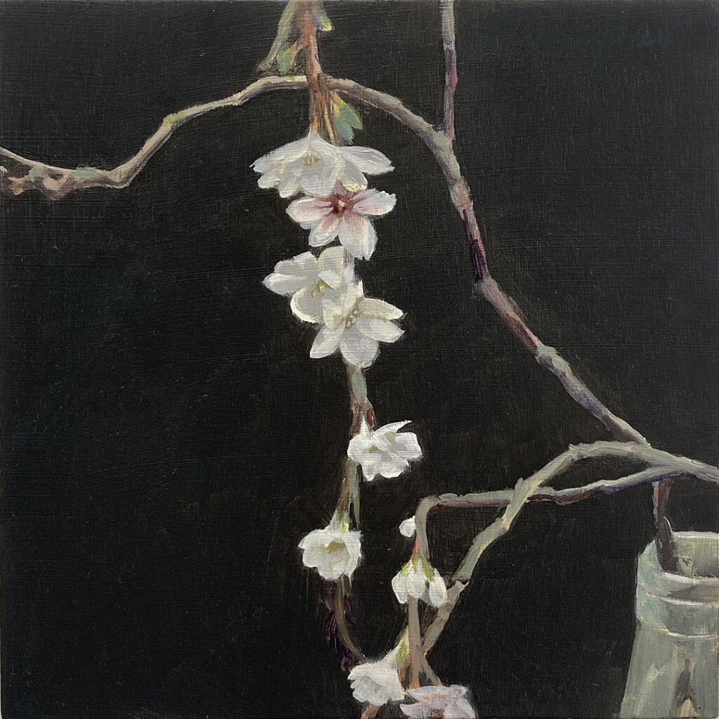 Small pale blossoms coming off a few highly coloured, thin branches, over a black background, with a section of the mouth of a milk bottle that holds the stems, in the bottom right hand corner