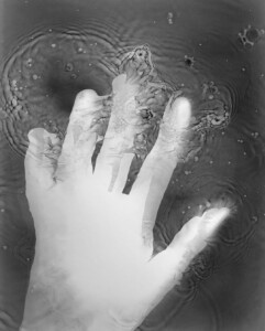 Black and white photogram of the inverted shadow of Kate's hand in the liquid photographic developer, creating movement and liquid patterns, enlarged