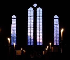 Photo of the dark interior of the church where the setting sun outside can be seen through the stained glass windows