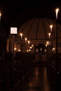 Photo showing the dark interior of the church with candles along the central aisle illuminating the gold boxes