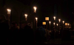 Photo showing the dark interior of the church, candles along the central aisle burning bright as the crowd pass through the installation