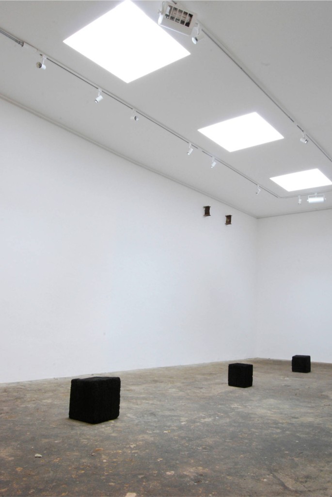 Photo documenting the interior of the exhibition space, which shows three large cubes of burnt oak arranged on the gallery floor in a line