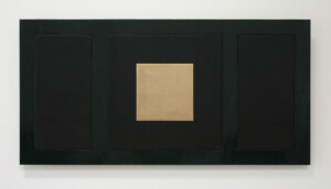 Facing view of the artwork "Memory of the dark", which has a small square gold shape in the middle, surrounded by an enamel black square, which is surrounded by a stained wood long larger rectangle.