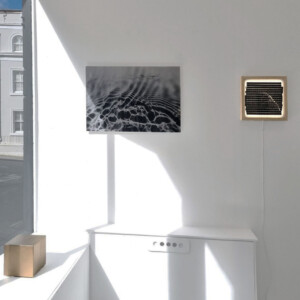 Artworks displayed in the gallery including a light-box, a enlarged photogram of wave patterns and a gold cube