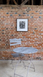 Framed artwork on brick wall with small garden table and chair in front