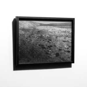 Black framed photograph of a rock and bolder studded terrain going away into the distance. A bit lunar-like.