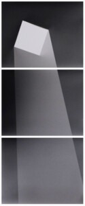 A tall set of three rectangles, one above the next, with a thin half inch gap between them. The image on the panels works as one and is of a crisp, white square floating in the top black space. From the white square there is a seeming projection of grey foggy light beaming down from the seeming square aperture. It widens as it shines downwards, like a beam of light coming into a square aperture of the ceiling.